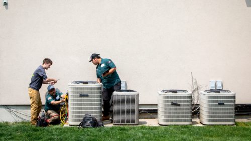 HomeWorks Energy team performs a cooling checkup at a customer's home, standing by a large air conditioner.