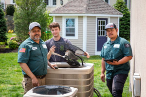 HomeWorks Energy team performs a cooling checkup at a customer's home, standing by a large air conditioner.