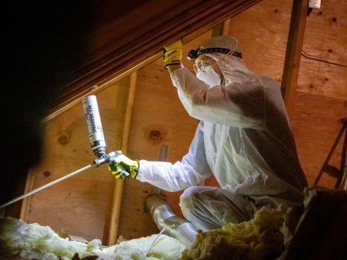 A man dressed in a white suit and gloves works on insulation, highlighting HomeWorks Energy's collaboration with Mass Save for home upgrades.